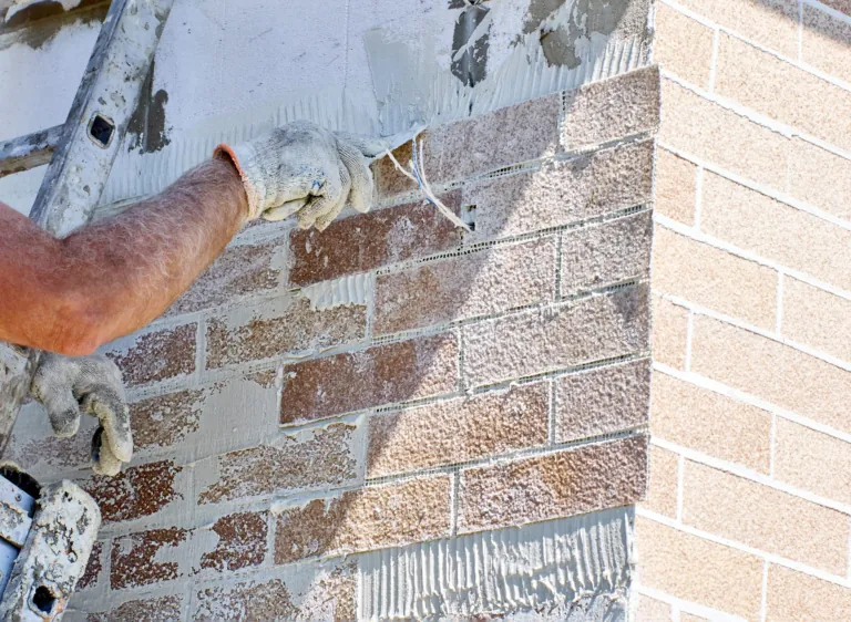 Main gantée appliquant un enduit sur un mur en pierre