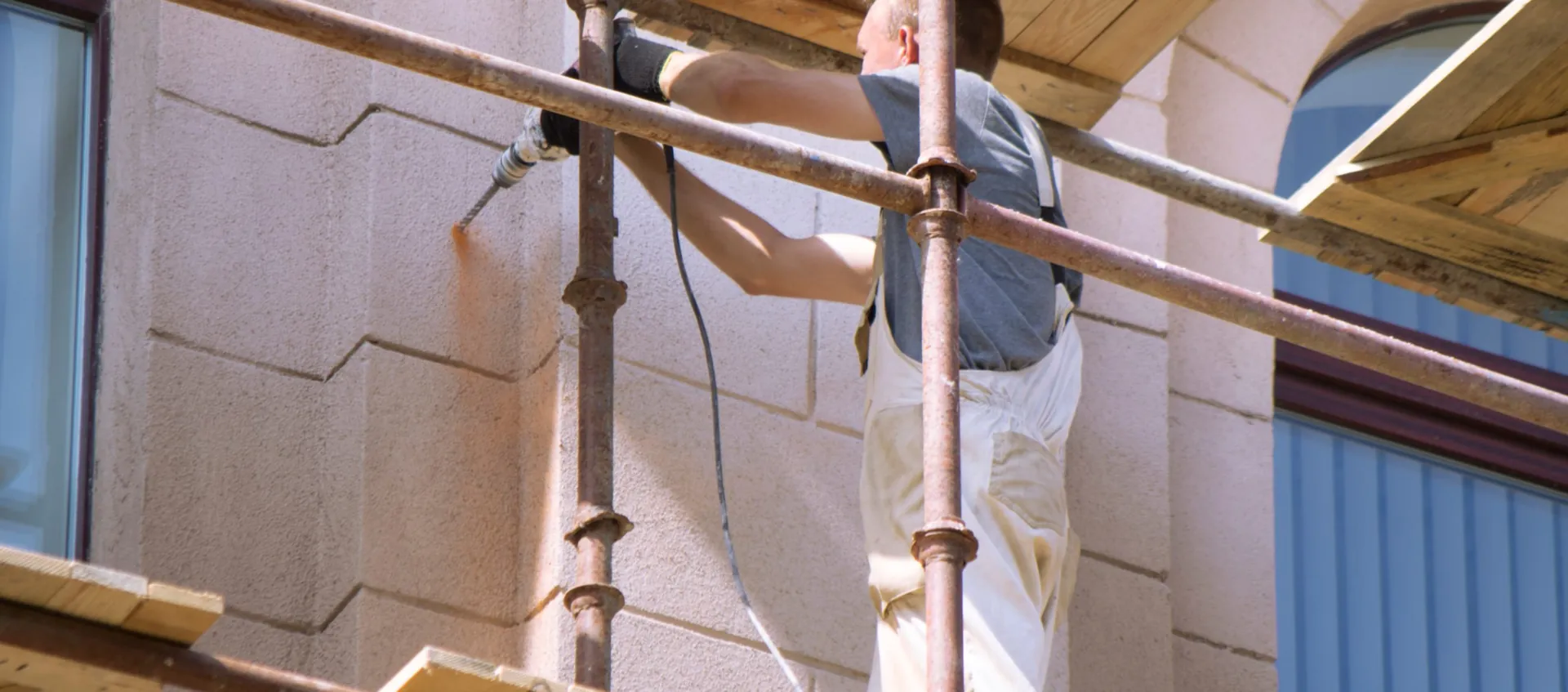 Façadier sur un échafaudage repeignant une façade en pierre