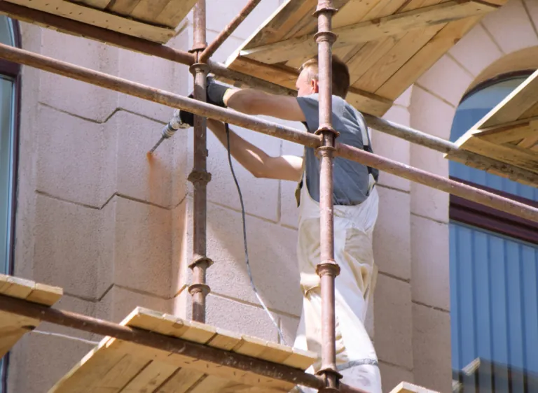 Façadier sur un échafaudage repeignant une façade en pierre