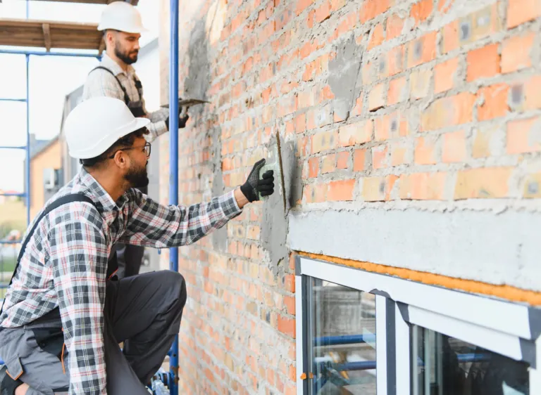 Deux façadiers appliquant un enduit sur un mur en briques