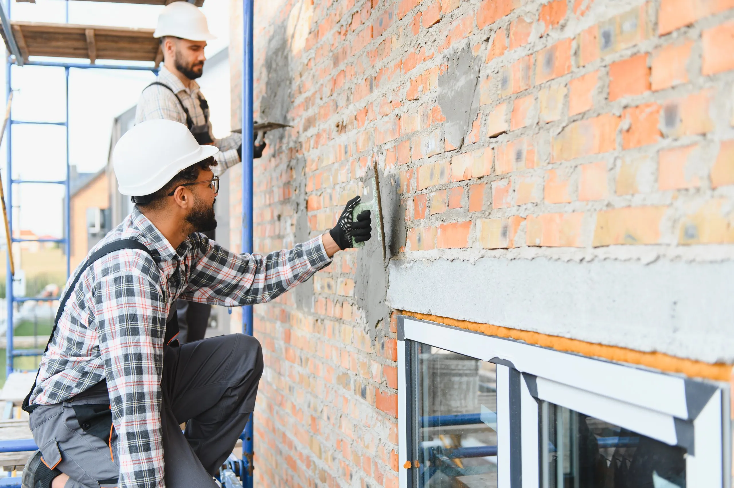 Deux façadiers appliquant un enduit sur un mur en briques
