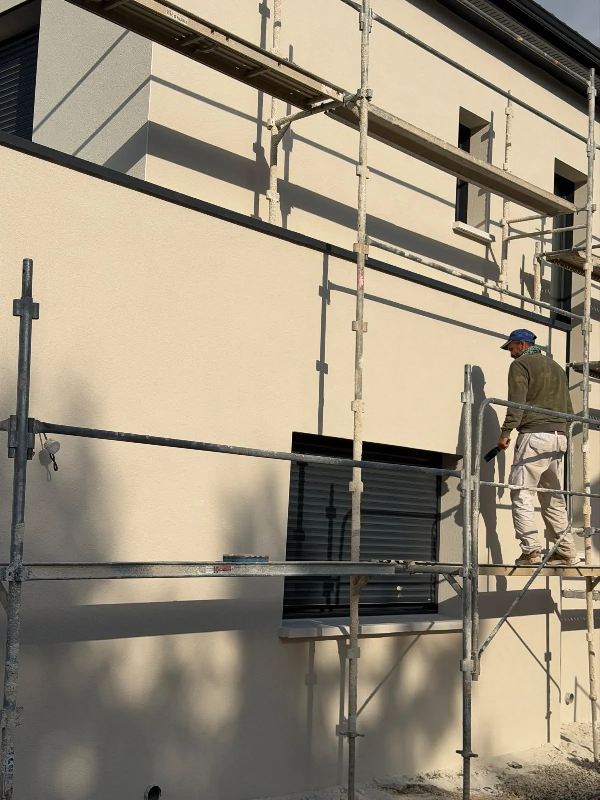 Ouvrier sur un échafaudage devant une façade beige en rénovation